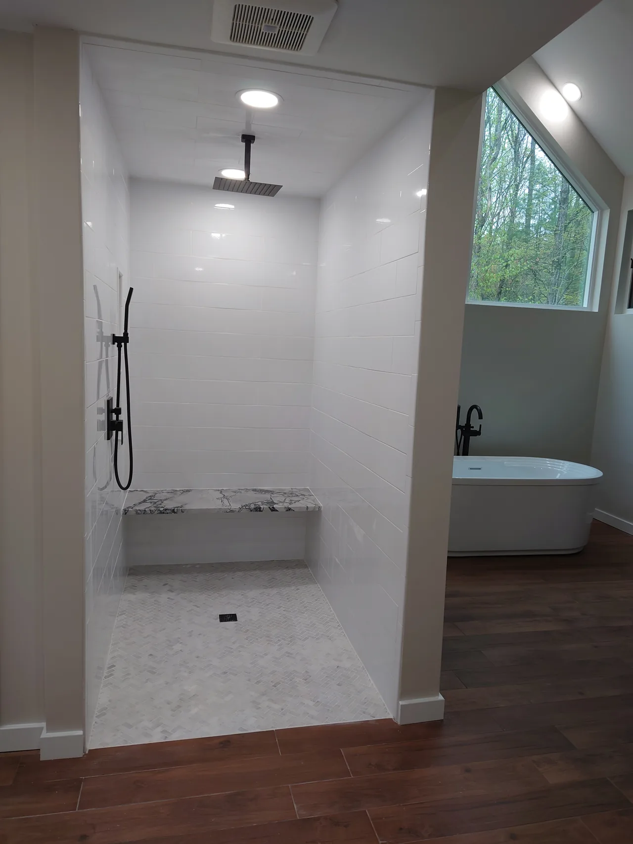 White tiled shower with dark fixtures and a built-in bench
