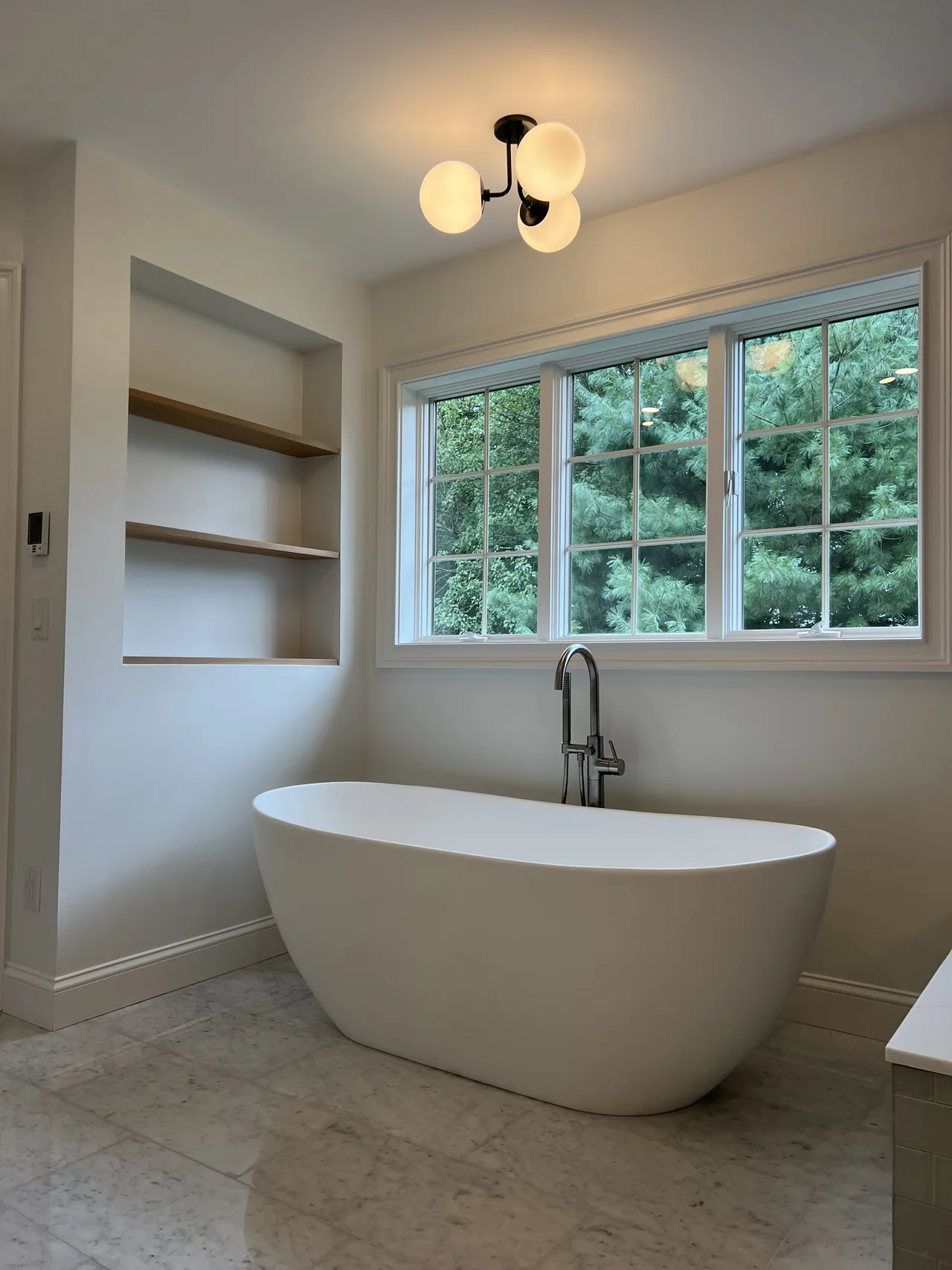 Recessed wood shelving beside a freestanding bathtub