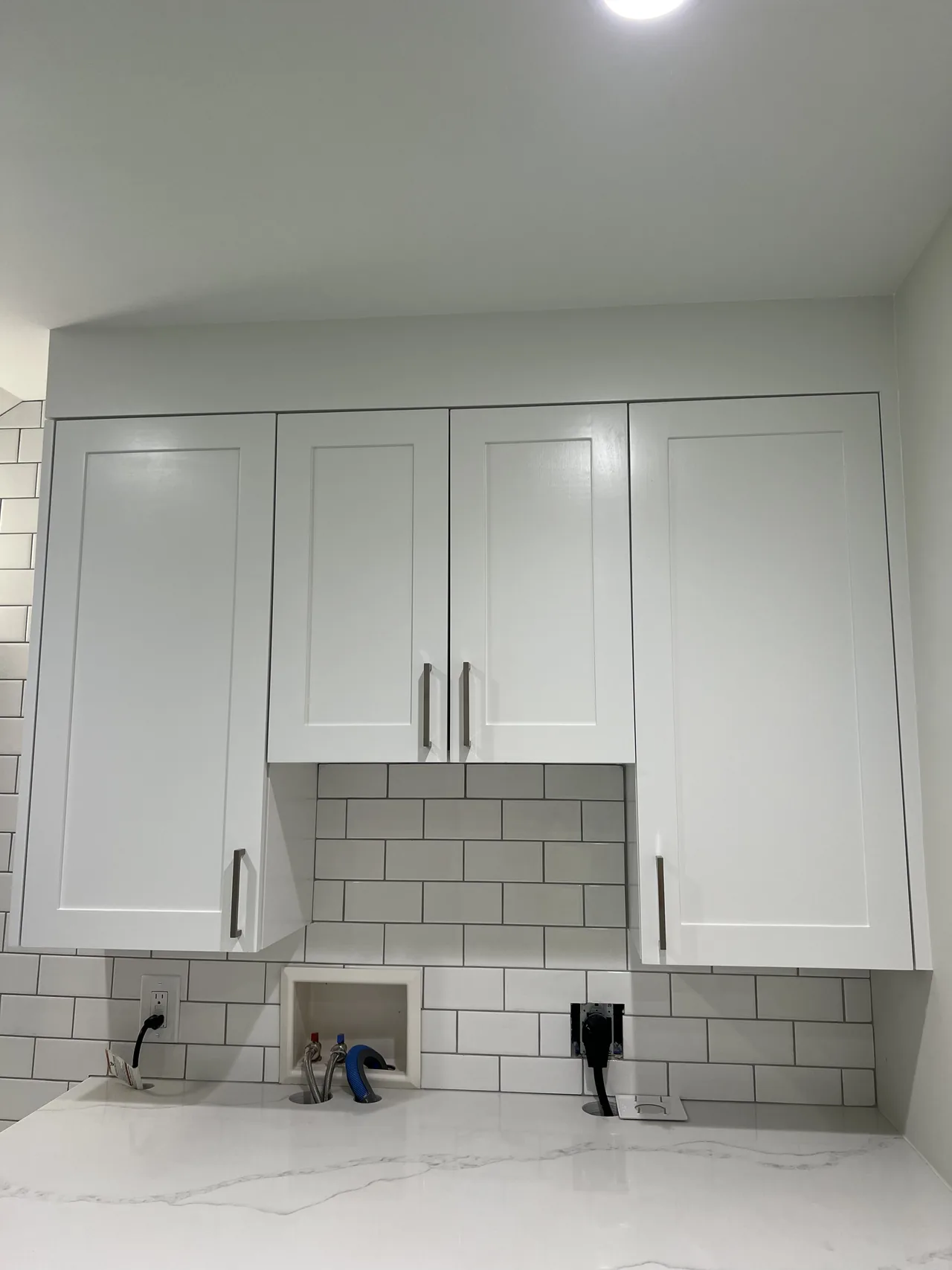 White laundry-room cabinets above a sink with a subway tile backsplash